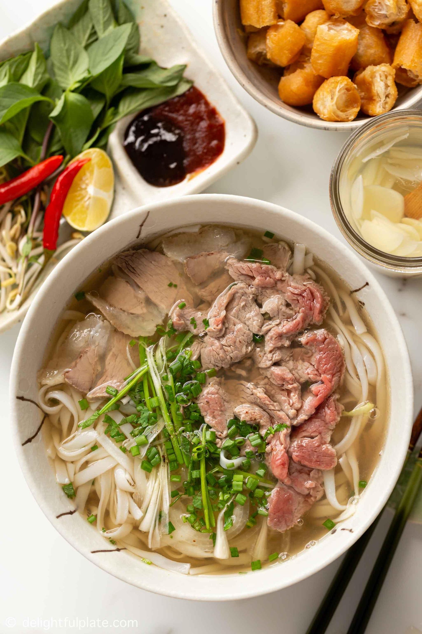 Vietnamesische Pho Suppe mit Rindfleisch, Reisnudeln, frischen Kräutern und Beilagen